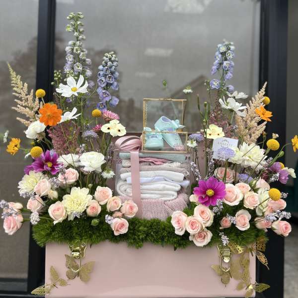 Pastel floral gift box with baby shoes and folded blankets
