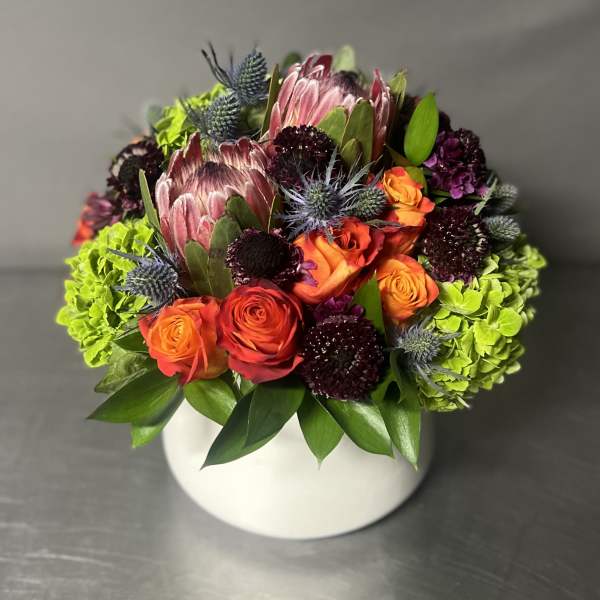 Bright mixed bouquet in a white round vase with orange roses and green hydrangeas