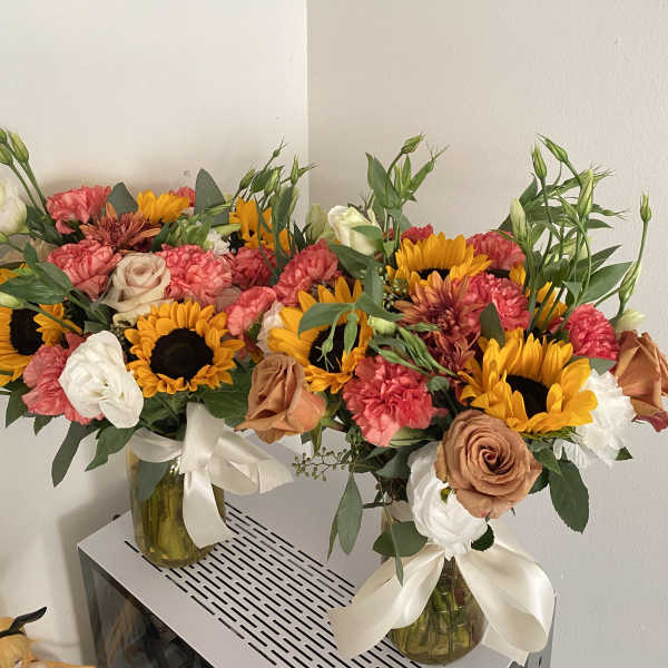 Two mixed flower arrangements in glass vases with sunflowers, roses, and carnations