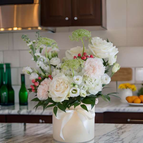 White and blush floral arrangement in a round box with a ribbon
