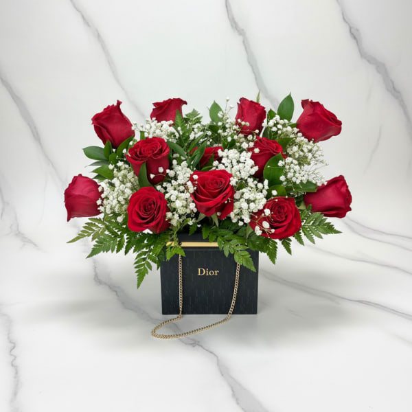 Red roses arranged in a black Dior gift box with a gold chain