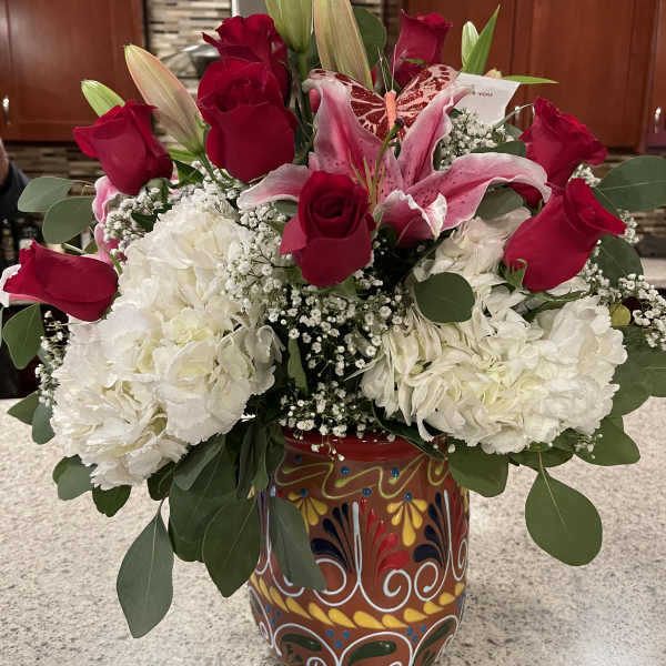 Red roses and pink lilies arranged with white blooms in a painted vase.