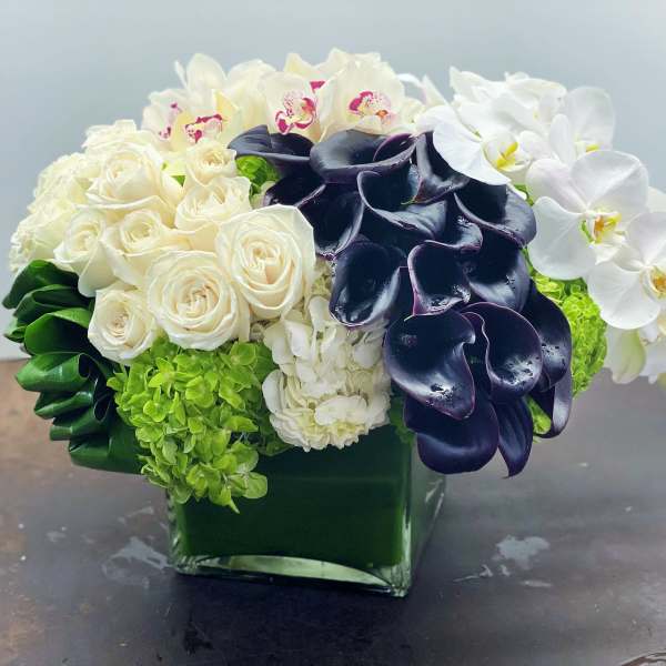 White roses, orchids, and dark calla lilies in a green glass vase
