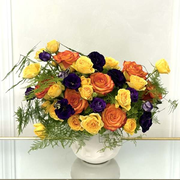 Bouquet of yellow, orange, and purple roses in a white vase