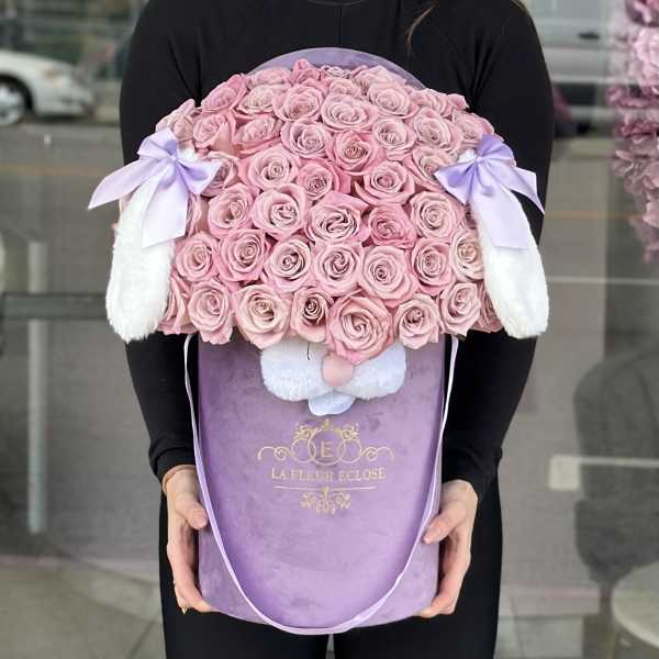 Pink roses arranged in a lavender gift box with white bunny ears and bows