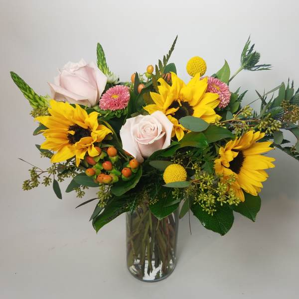 Bouquet of sunflowers and pale pink roses in a glass vase