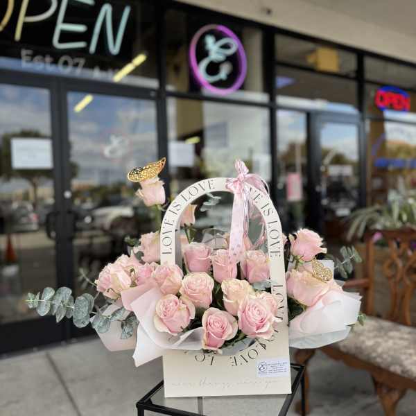 Pink roses arranged in a white basket with a LOVE ribbon