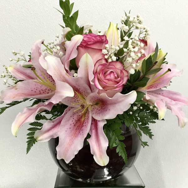 Pink lilies and roses arranged in a dark glass vase