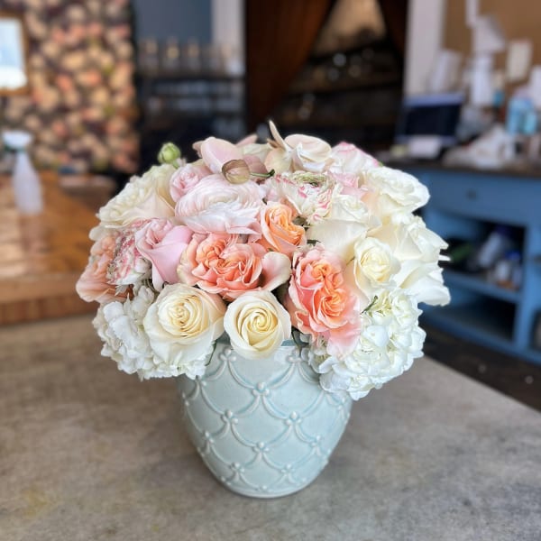 Pastel roses and white blooms arranged in a light blue vase