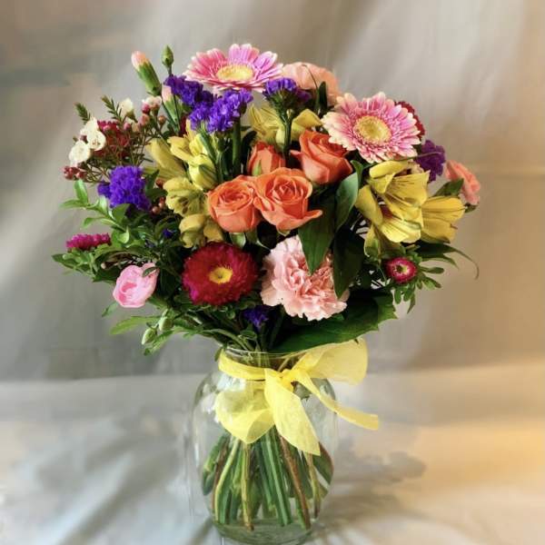 Mixed bouquet of pink, orange, yellow, and purple flowers in a glass vase