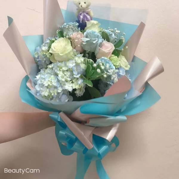 Pastel bouquet with roses and hydrangeas, topped with a small teddy bear