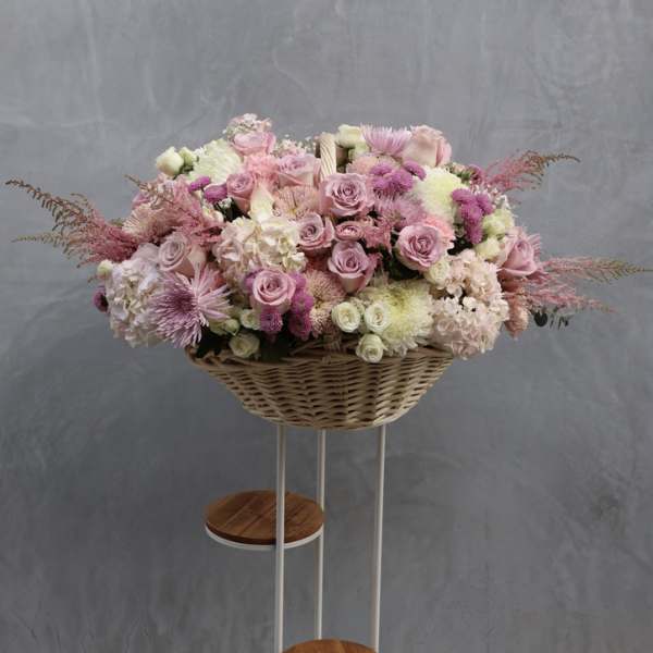 Large pink and white floral arrangement in a wicker basket on a stand