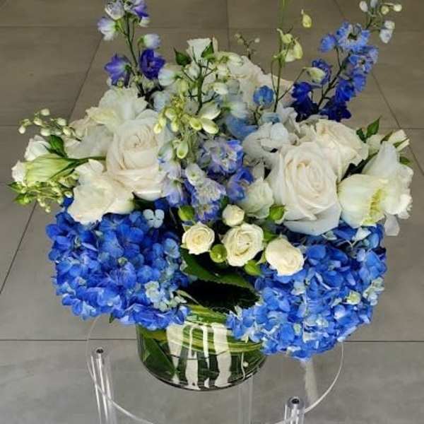 Low arrangement of white roses and blue hydrangeas in a clear glass vase.