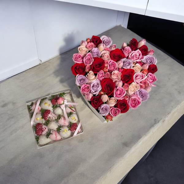 Heart-shaped box of pink and red roses beside a box of chocolate-covered strawberries