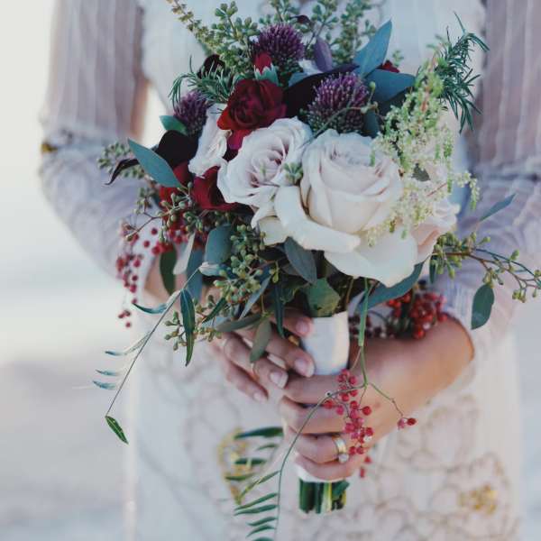 Bride holding a bouquet of white and red roses with greenery
