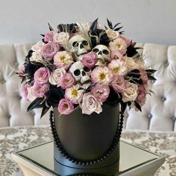 Pink and cream flowers arranged with decorative skulls in a black hatbox