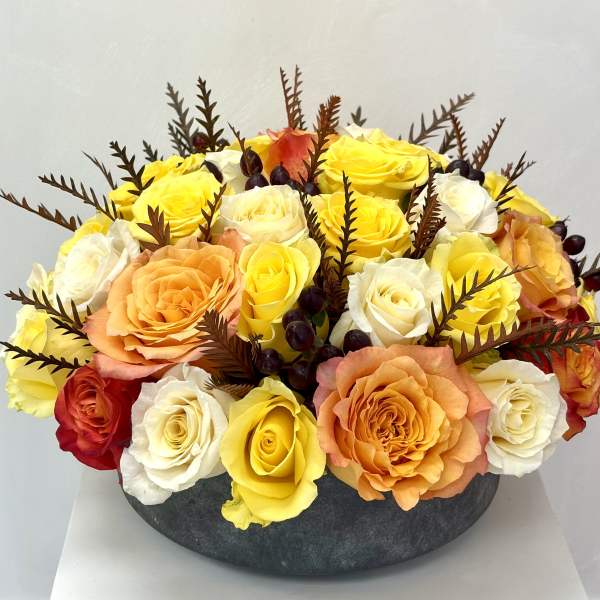 Round arrangement of yellow, white, orange, and red roses in a dark vase