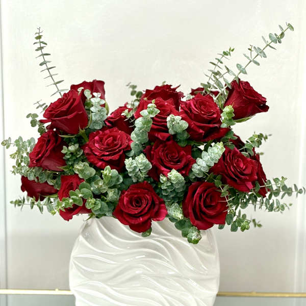 Arrangement of red roses and eucalyptus in a textured white ceramic vase