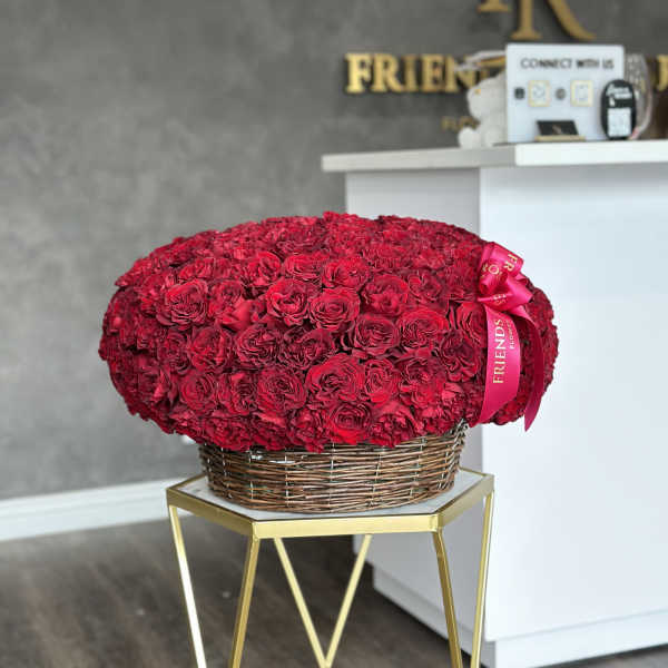 Large red rose arrangement in a wicker basket with a pink ribbon