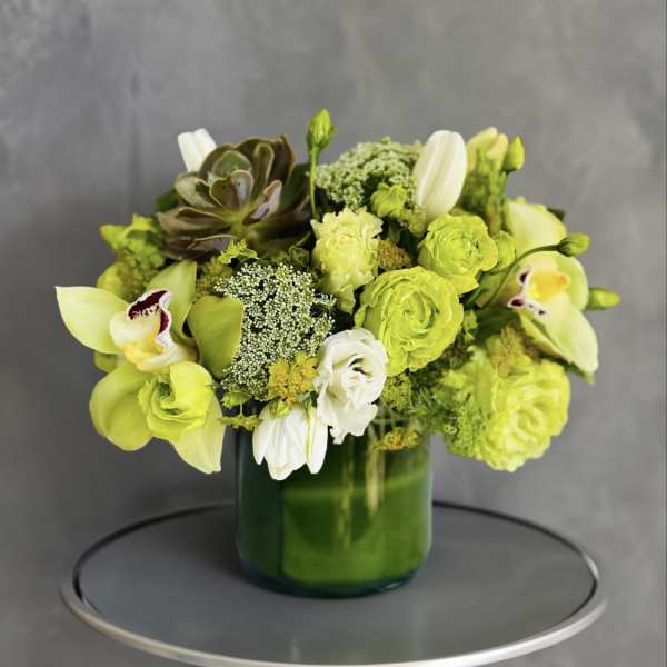 Green and white floral arrangement in a green glass vase