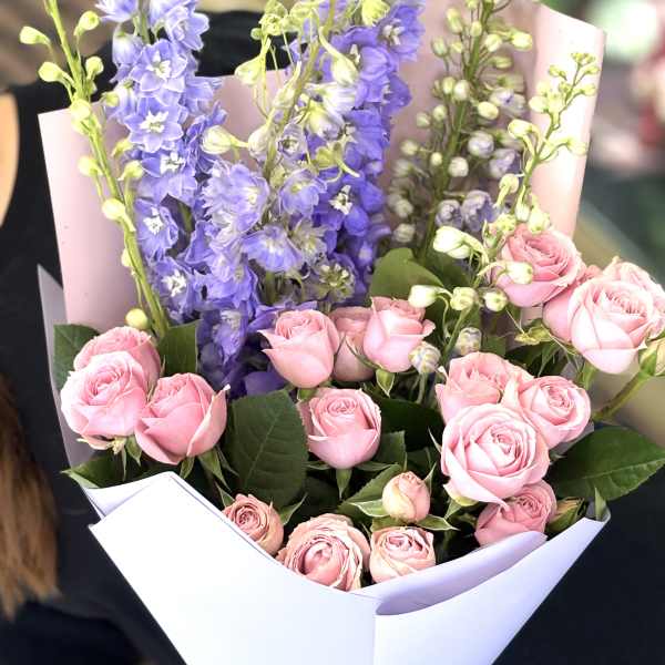Bouquet of pink roses and purple delphinium in white wrap