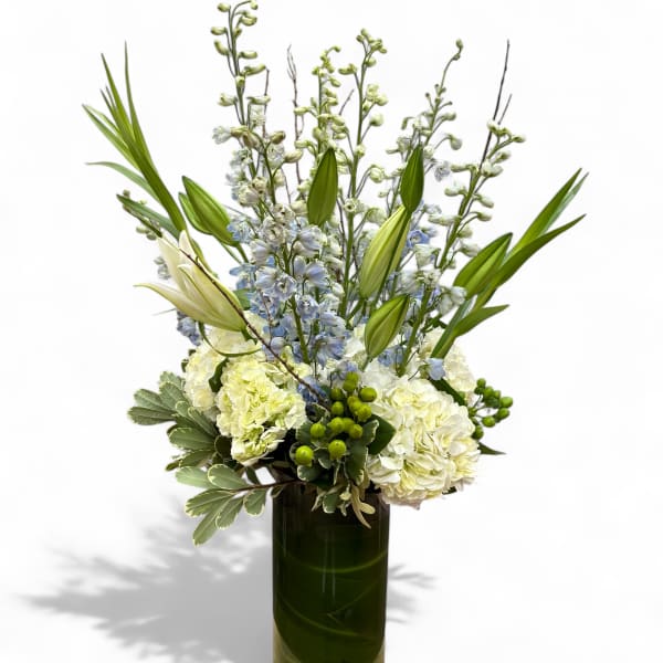 Tall white and pale blue floral arrangement in a dark glass vase