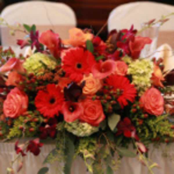 Low centerpiece of red gerbera daisies, peach roses, and green hydrangeas in a lush arrangement