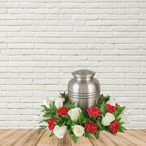 White roses and red carnations arranged around a silver urn.