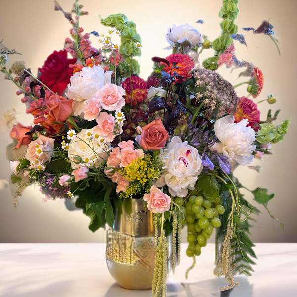Large mixed floral arrangement in a gold vase with pink, white, and green blooms