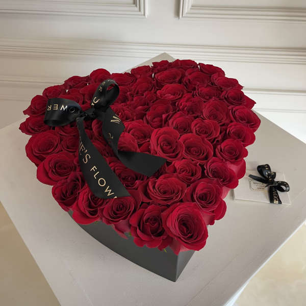 Heart-shaped box filled with red roses and a black ribbon