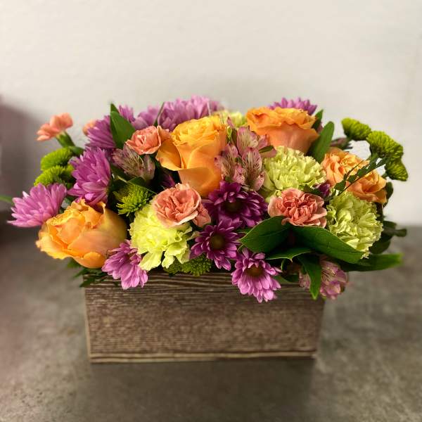 Mixed bouquet of orange roses, purple daisies, and carnations in a rectangular box