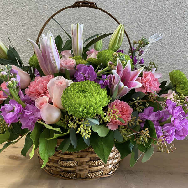 Basket arrangement with pink lilies, roses, carnations, and purple blooms