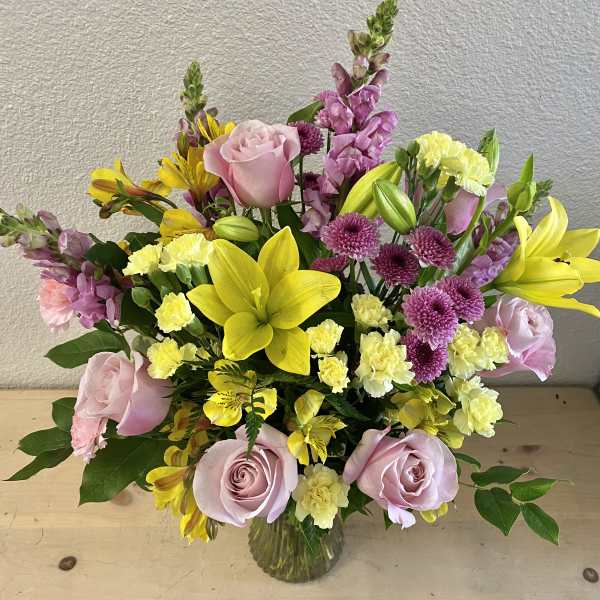 Pink roses, yellow lilies, and purple flowers in a glass vase