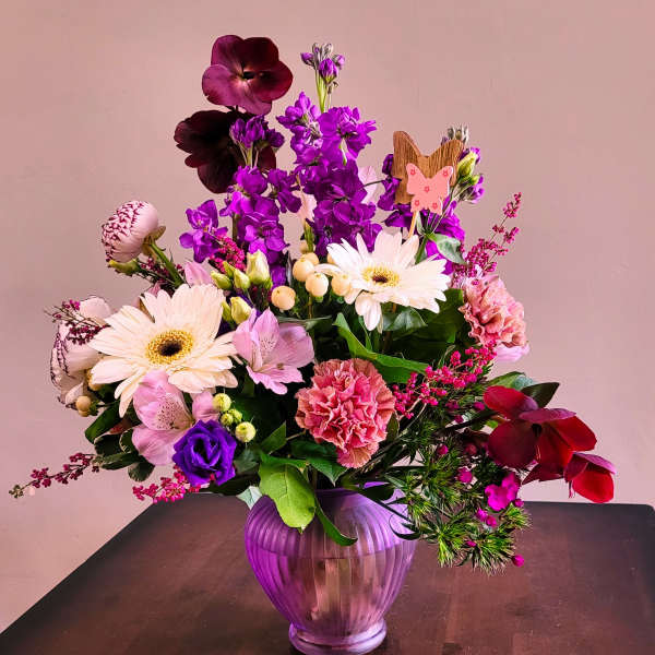 Mixed pink, purple, and white flower arrangement in a purple glass vase with a small butterfly pick