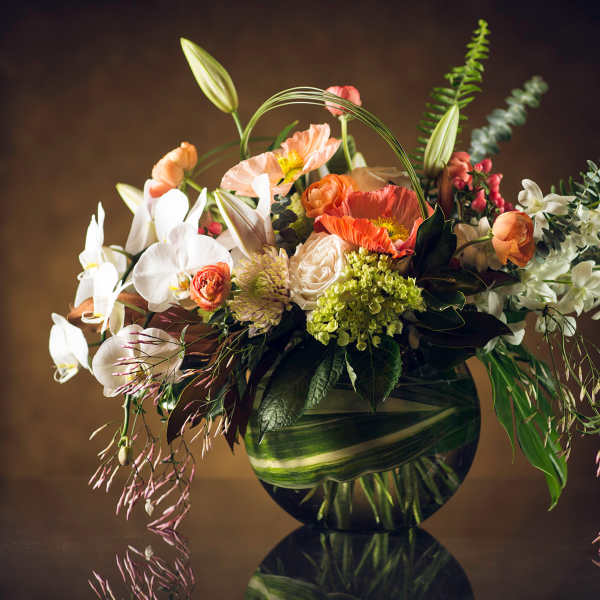 Mixed floral arrangement in a round glass vase with white orchids and orange poppies