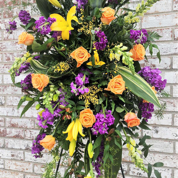 Standing floral spray with orange roses, yellow lilies, and purple blooms