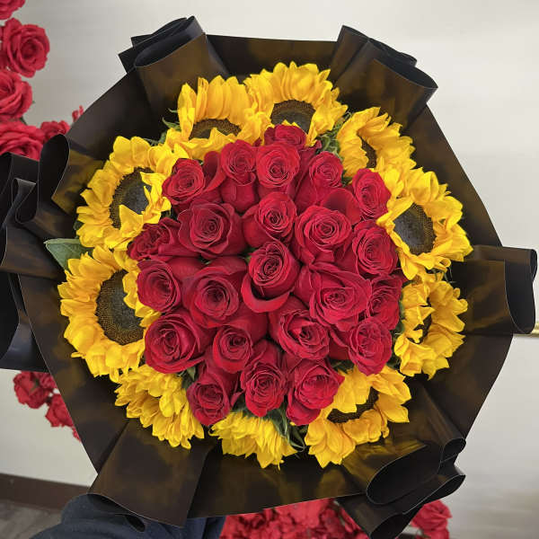 Bouquet of red roses surrounded by yellow sunflowers in black wrap