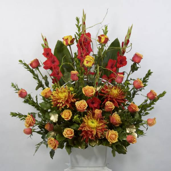Tall arrangement of red and orange flowers in a white container