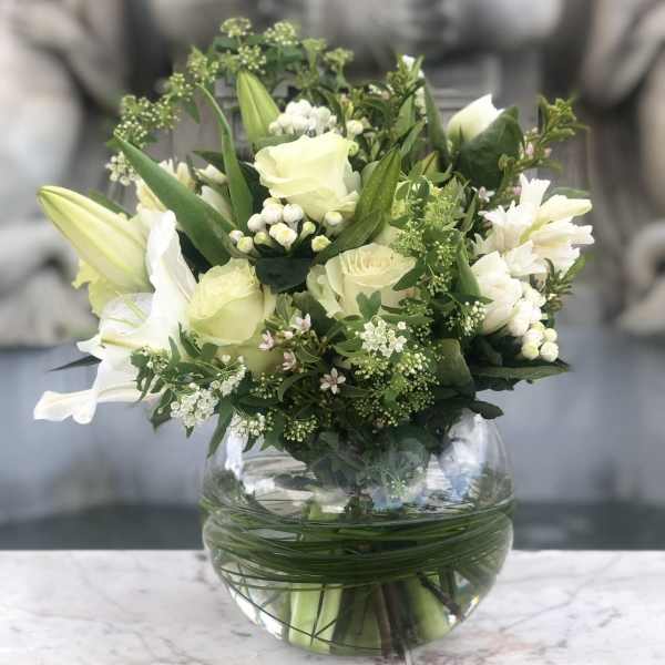 White and pale green floral arrangement in a round glass vase