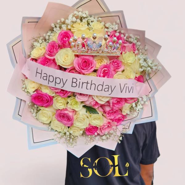 Bouquet of pink and pale yellow roses with a birthday ribbon and crown