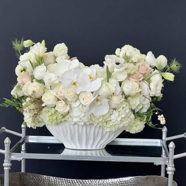White floral arrangement in a white pedestal vase with pale blush accents