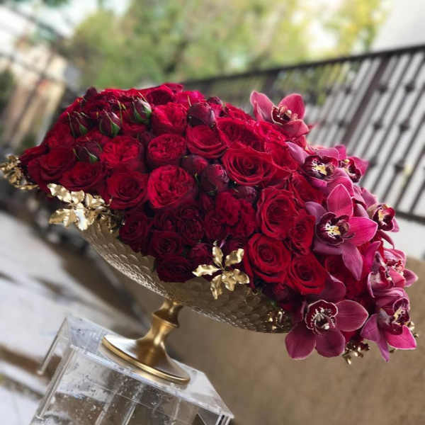 Red rose arrangement with pink orchids in a gold pedestal bowl