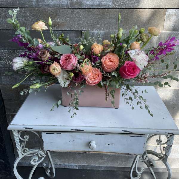 Mixed bouquet of pink, peach, and white flowers in a pink rectangular vase