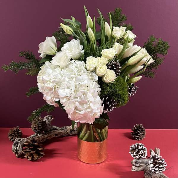 White floral arrangement in a copper vase with pinecones and evergreen branches