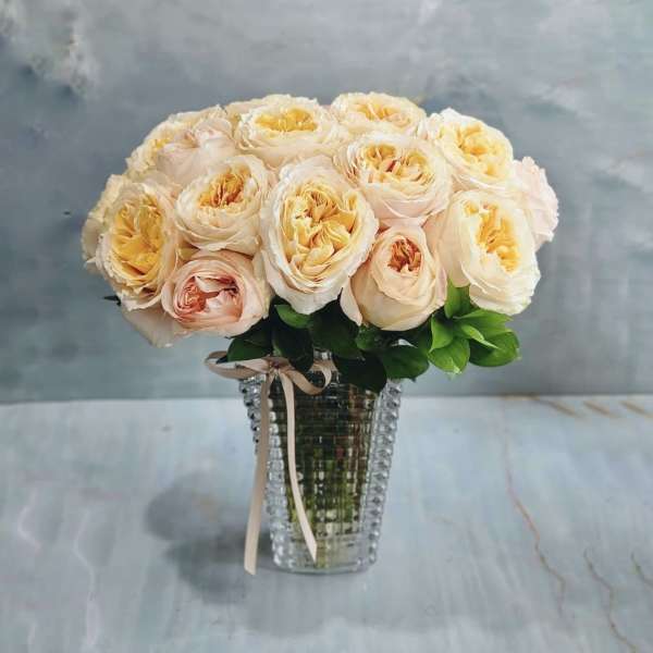 Peach and cream roses in a clear glass vase with a ribbon