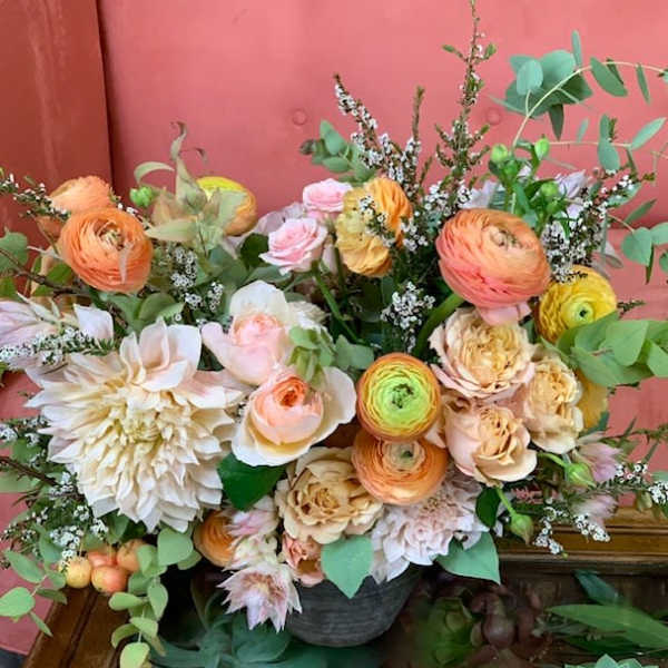 Mixed bouquet of peach, pink, and cream flowers in a dark container