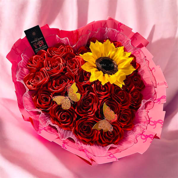 Bouquet of red roses with a yellow sunflower accent in pink wrapping