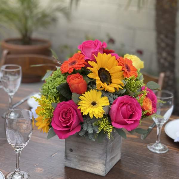 Bright mixed bouquet in a square wooden vase on a table