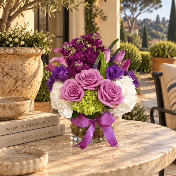 Purple and pink flower arrangement in a clear glass vase with a ribbon