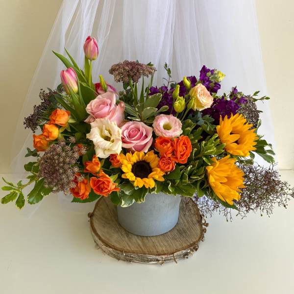 Mixed bouquet with roses, tulips, sunflowers, and purple blooms in a gray container
